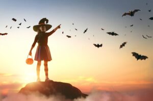 Young girl on a mountain top wearing a whitch hat and has bats all around her - image